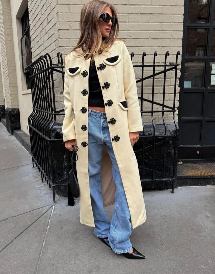 Long cream coat with black closures, jeans and pointed shoes