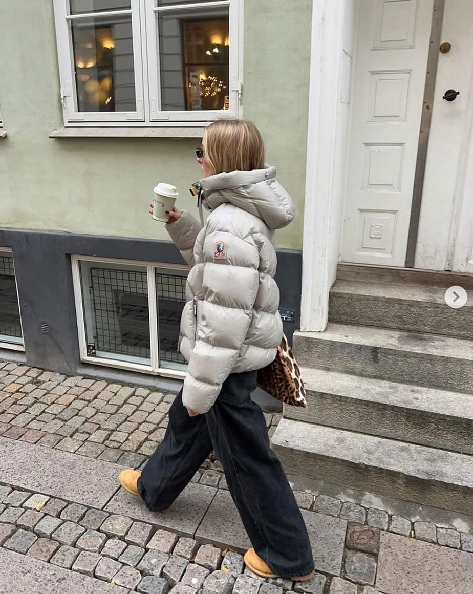 Pale gray hooded puffer with black wide trousers and tan shoes