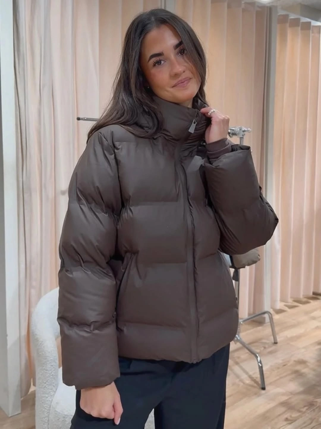 Taupe brown short padded jacket with dark trousers indoors
