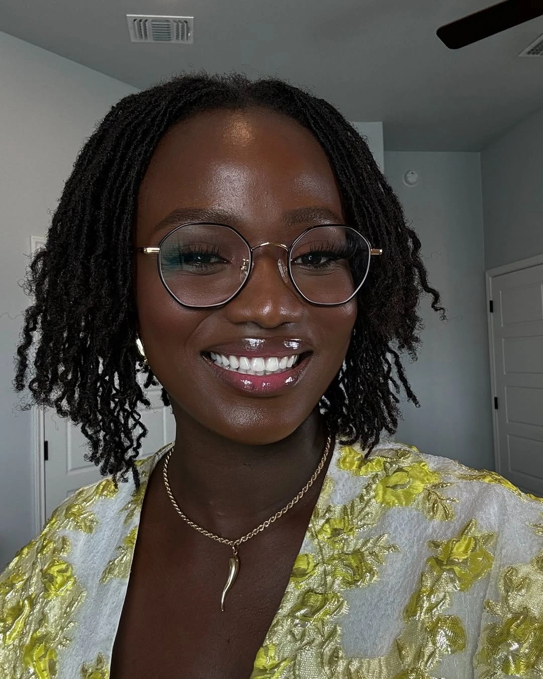 Short dark loc-like lengths with round glasses and yellow floral top