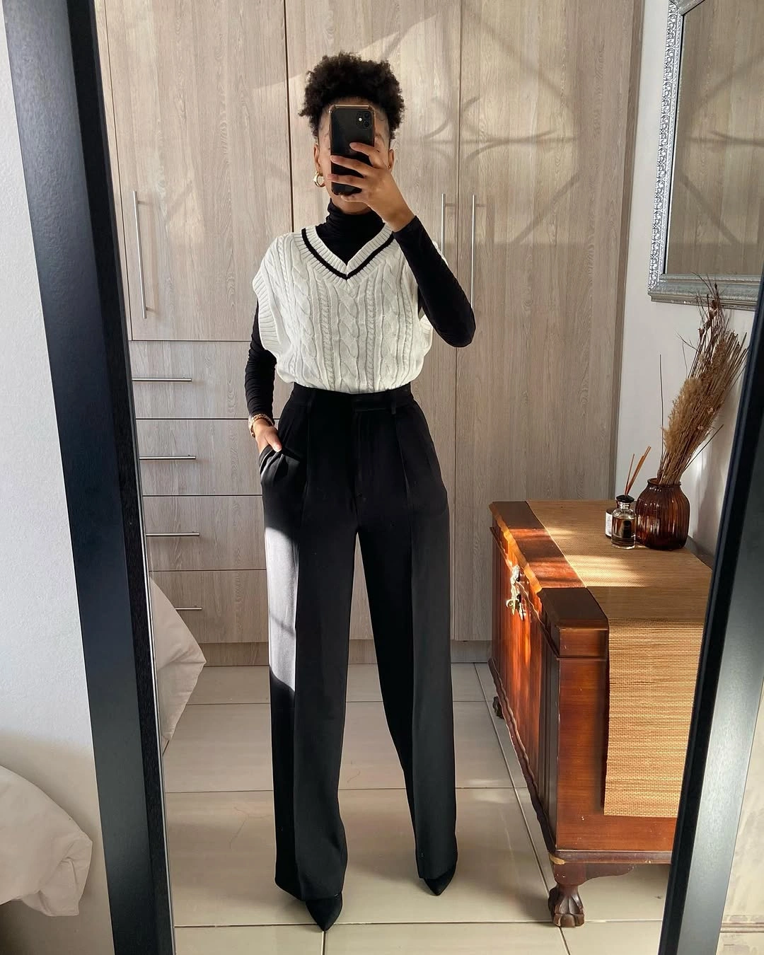 Cream cable-knit sleeveless sweater over black base and wide trousers
