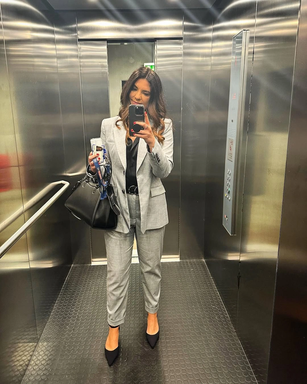 Woman in gray suit with black belt, pumps and handbag