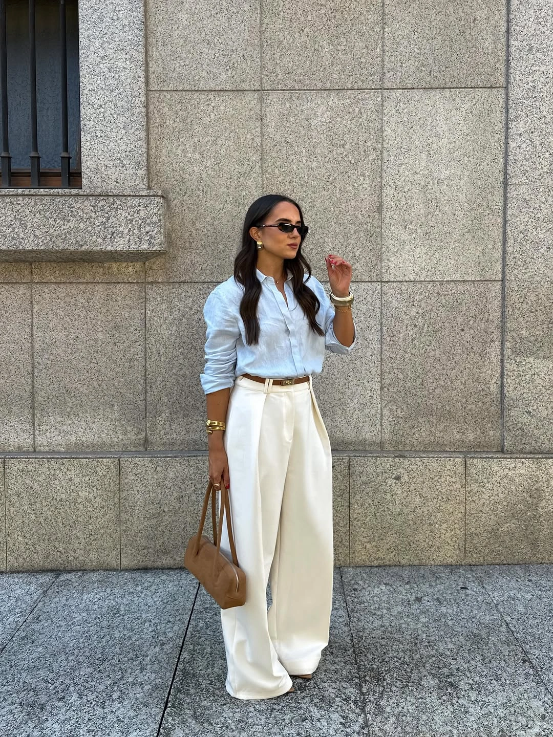 Blue button-down shirt with cream wide trousers and tan handbag