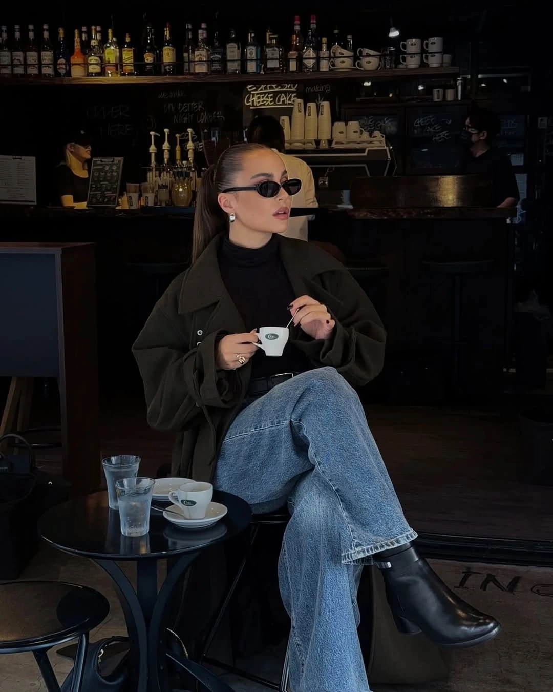 Dark high-neck top, olive outer layer, jeans and ankle boots
