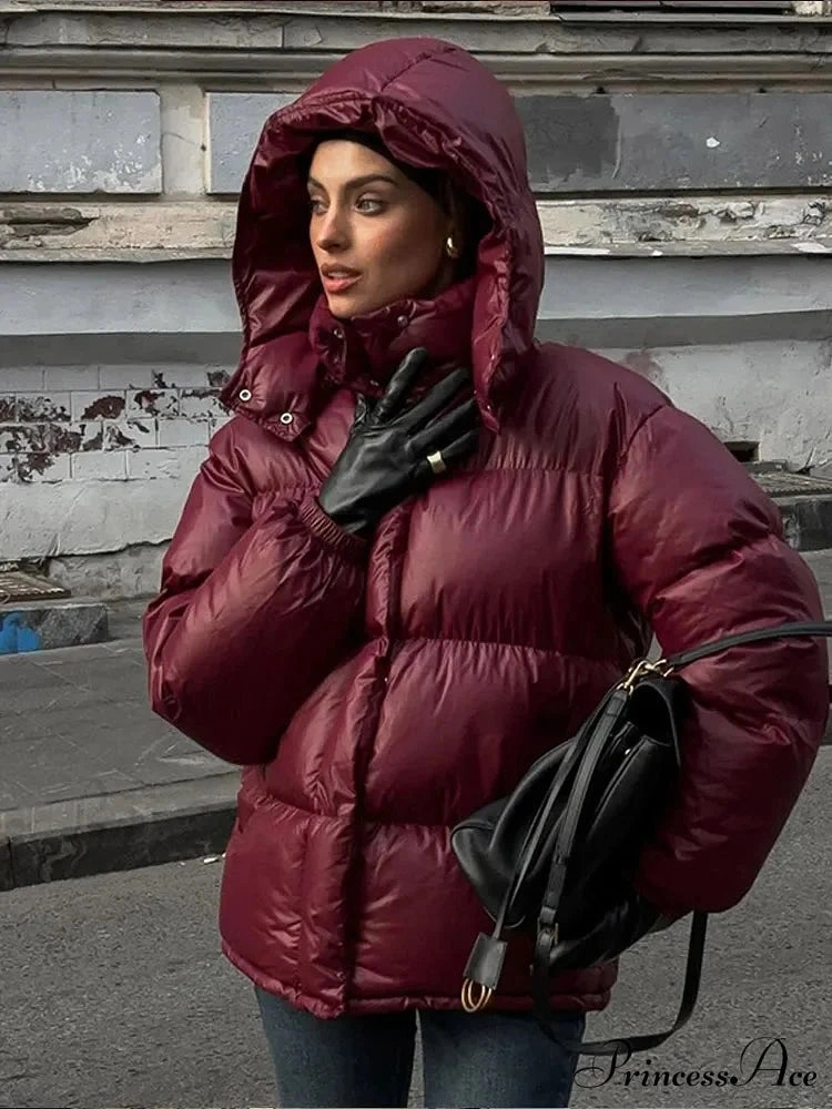 Glossy burgundy hooded puffer with black gloves and shoulder bag