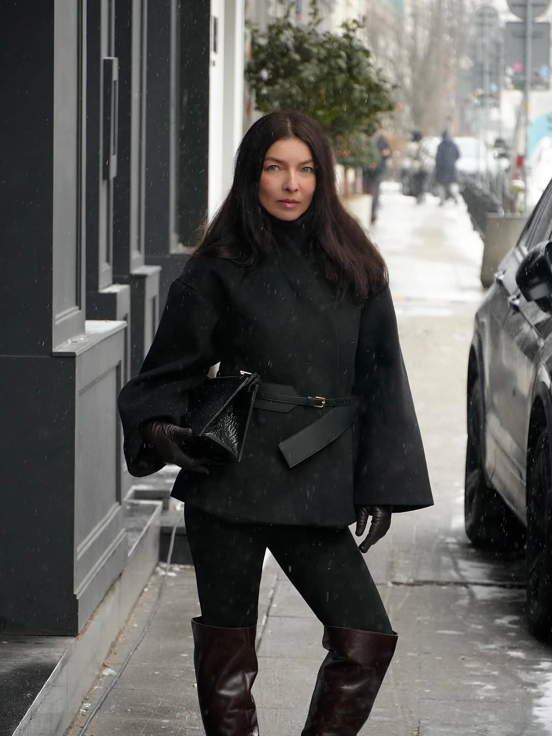 Black belted jacket with dark trousers and brown knee-high boots