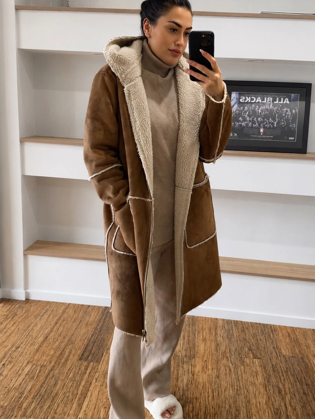 Brown lined coat over beige turtleneck and pale trousers