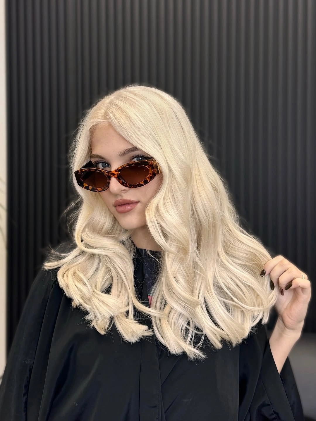Pale blonde wavy hair against dark clothing and wall