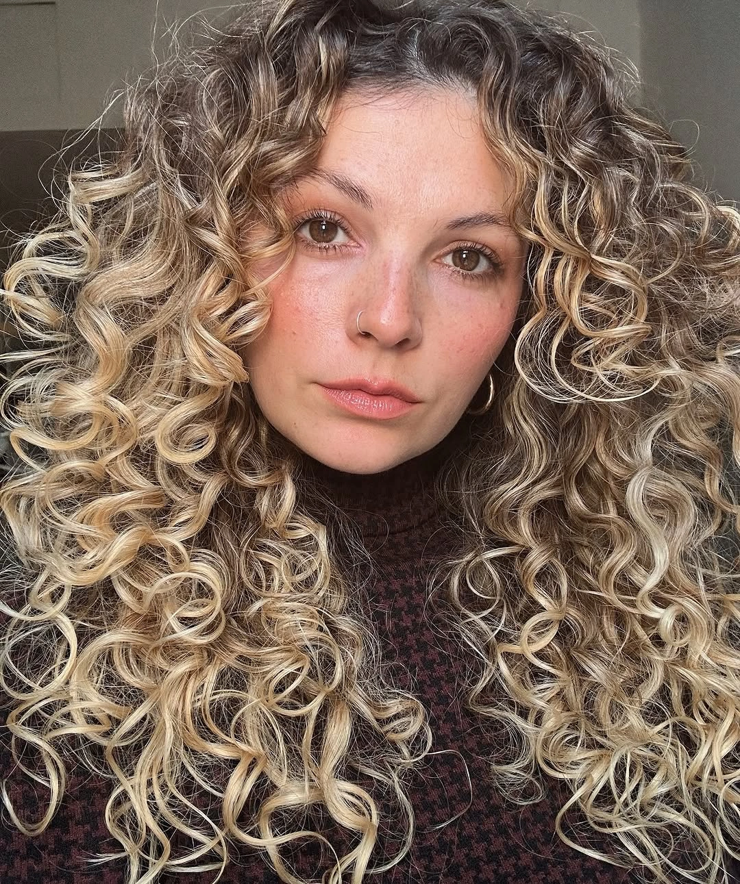 Tight blonde curls with darker roots and beige-gold tones