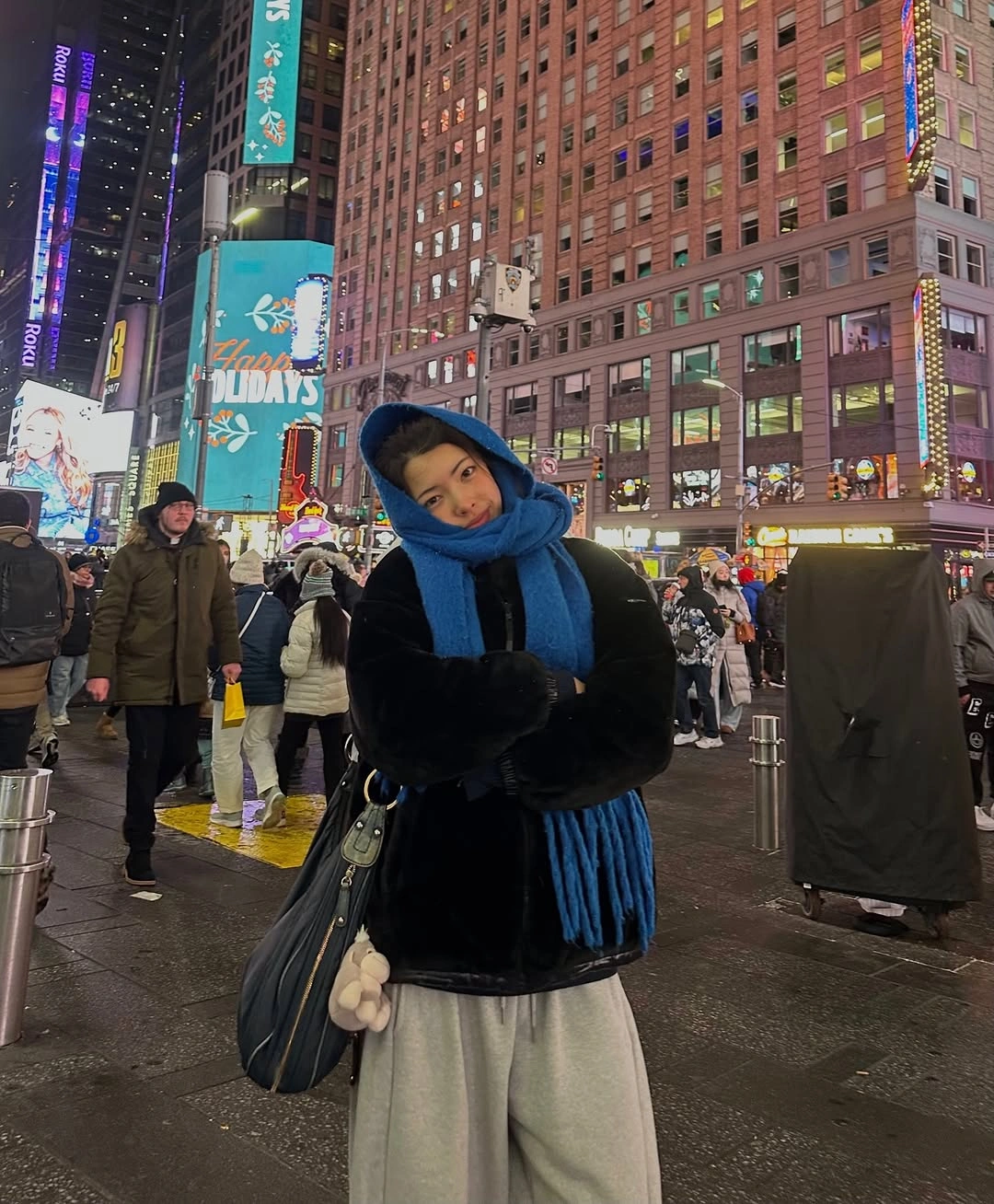 Woman in black jacket, blue scarf, and loose gray trousers