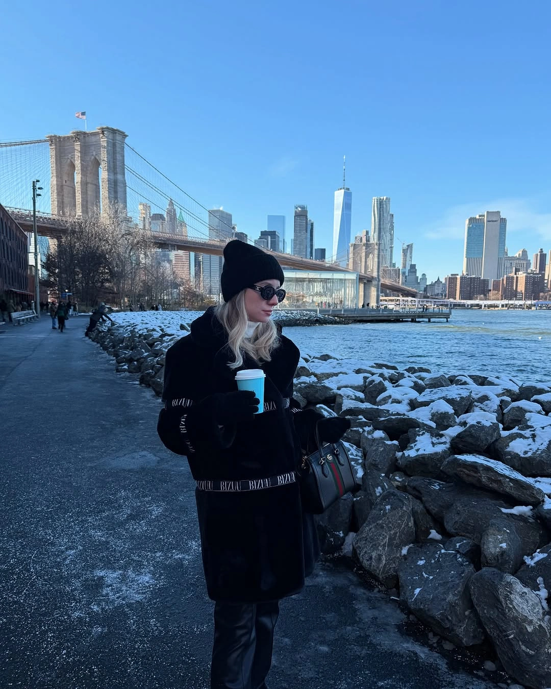 Woman in long black coat and beanie beside snowy waterfront