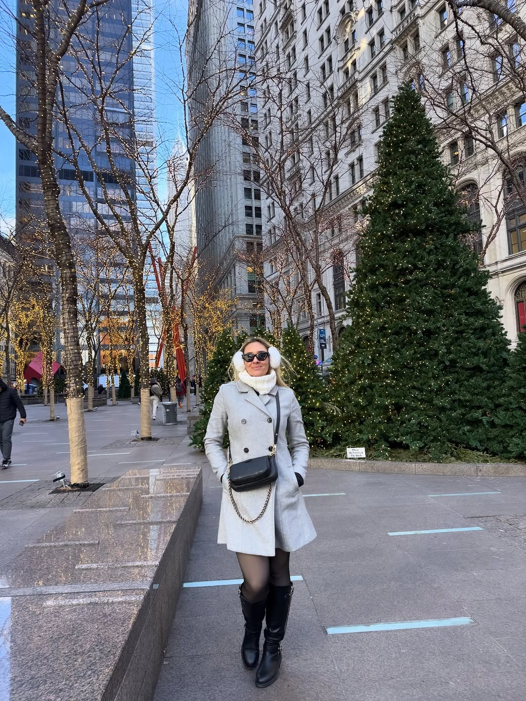 Woman in light gray coat, cream scarf, and tall black boots