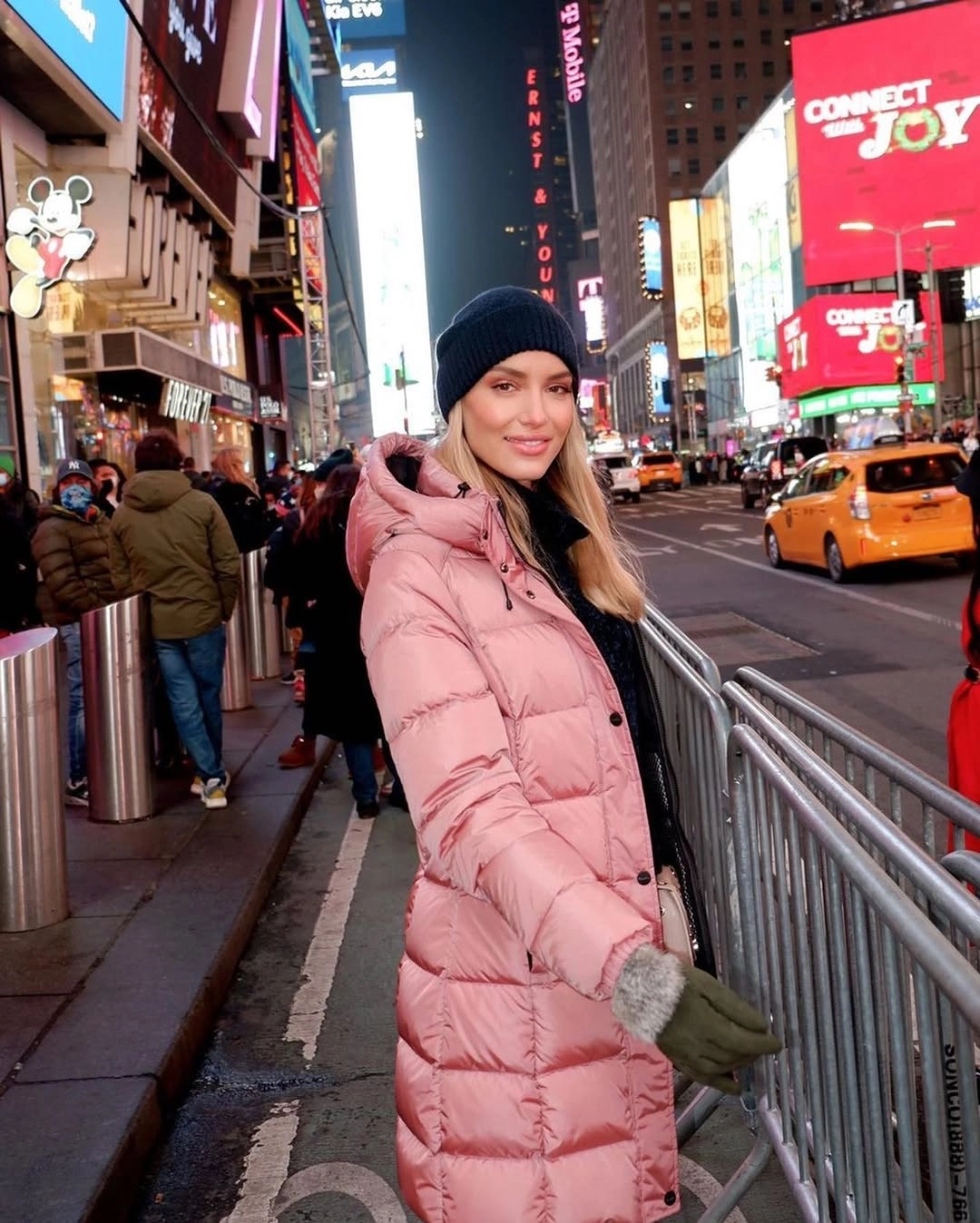 Woman in long pink puffer and black beanie on illuminated street