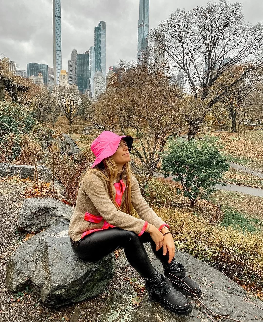 Woman in beige knit layer, pink hood, and black leggings