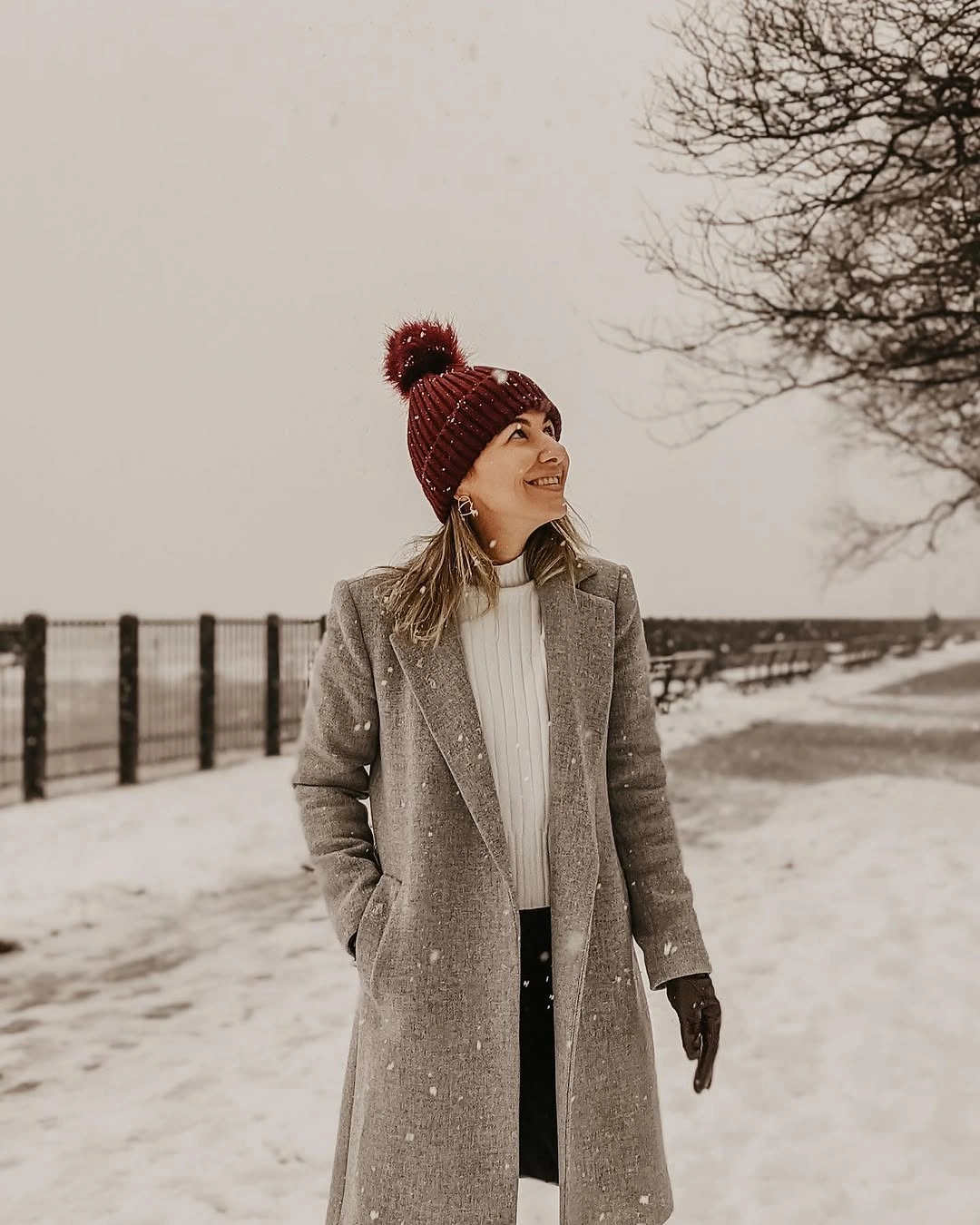 Woman in long gray coat and burgundy beanie on snowy path