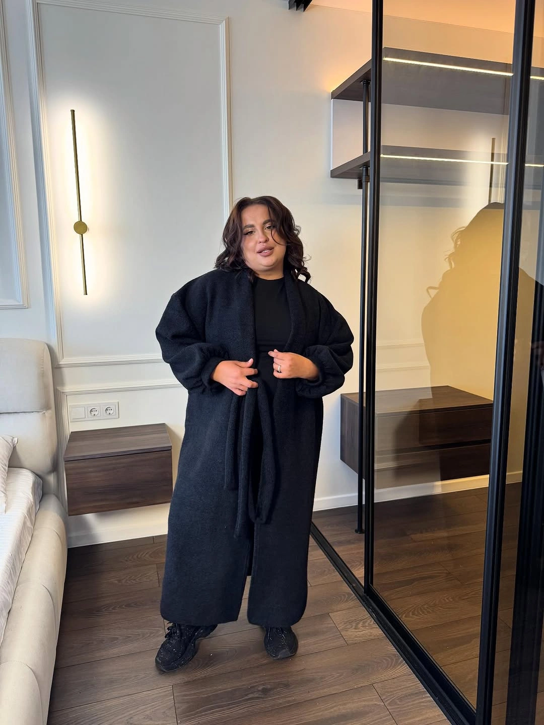 Long dark open outer layer over black outfit indoors