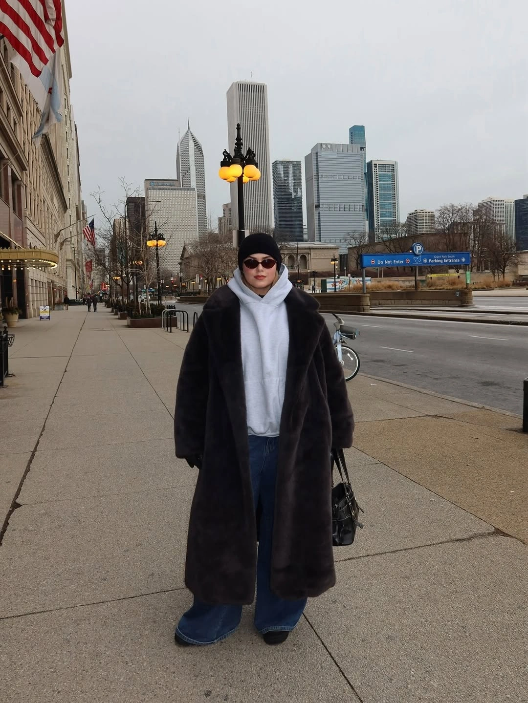 Long dark plush-looking coat over gray hoodie and jeans