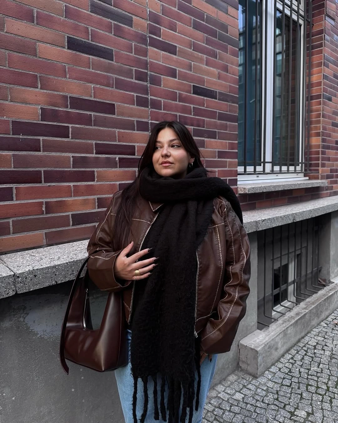 Brown leather-look jacket with large black scarf and jeans