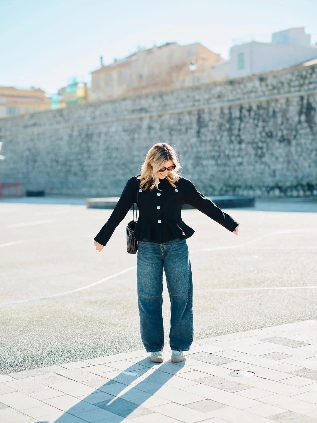 fitted black buttoned top with loose blue jeans white sneakers and dark bag