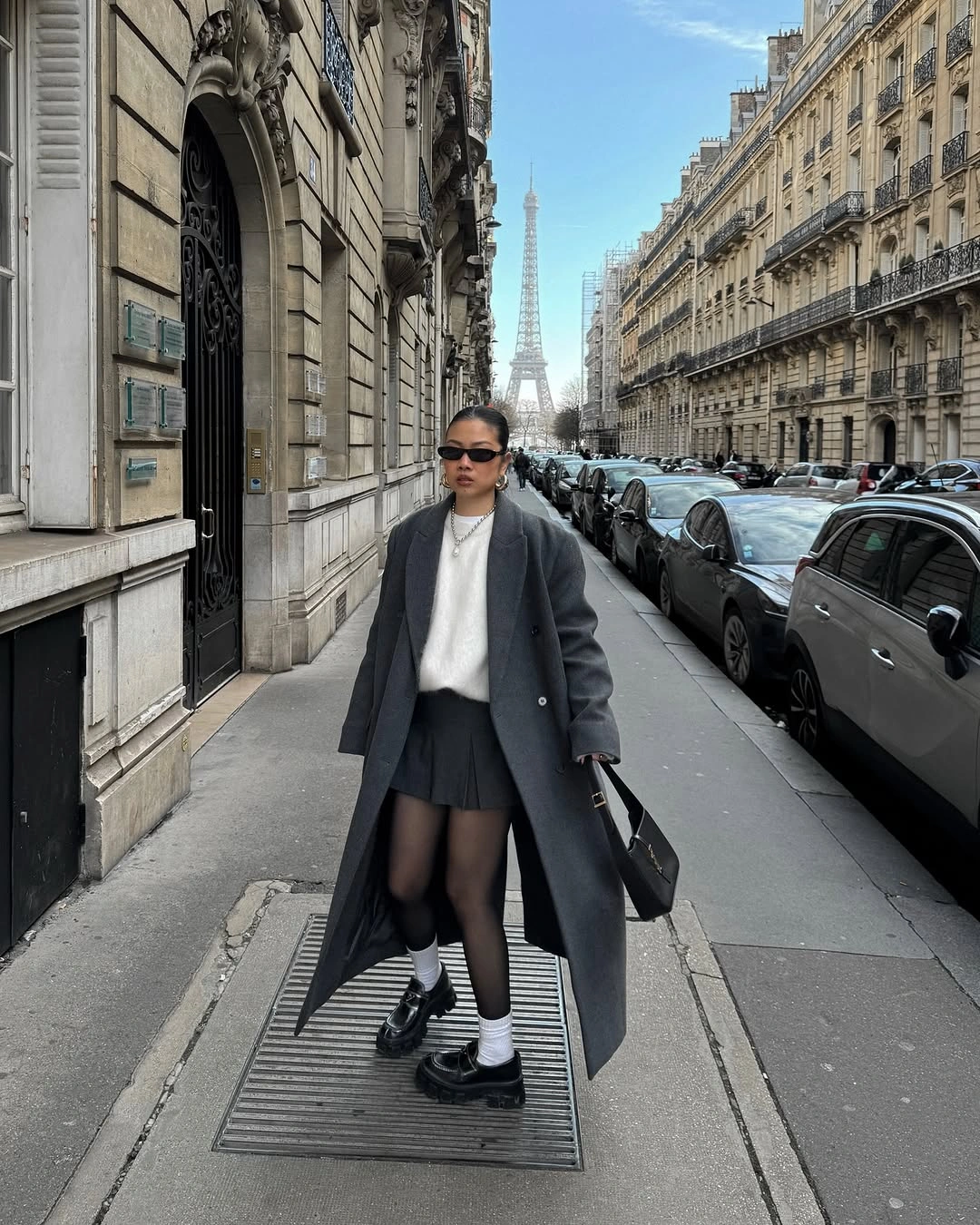 long charcoal coat with white sweater pleated black mini skirt tights socks and loafers