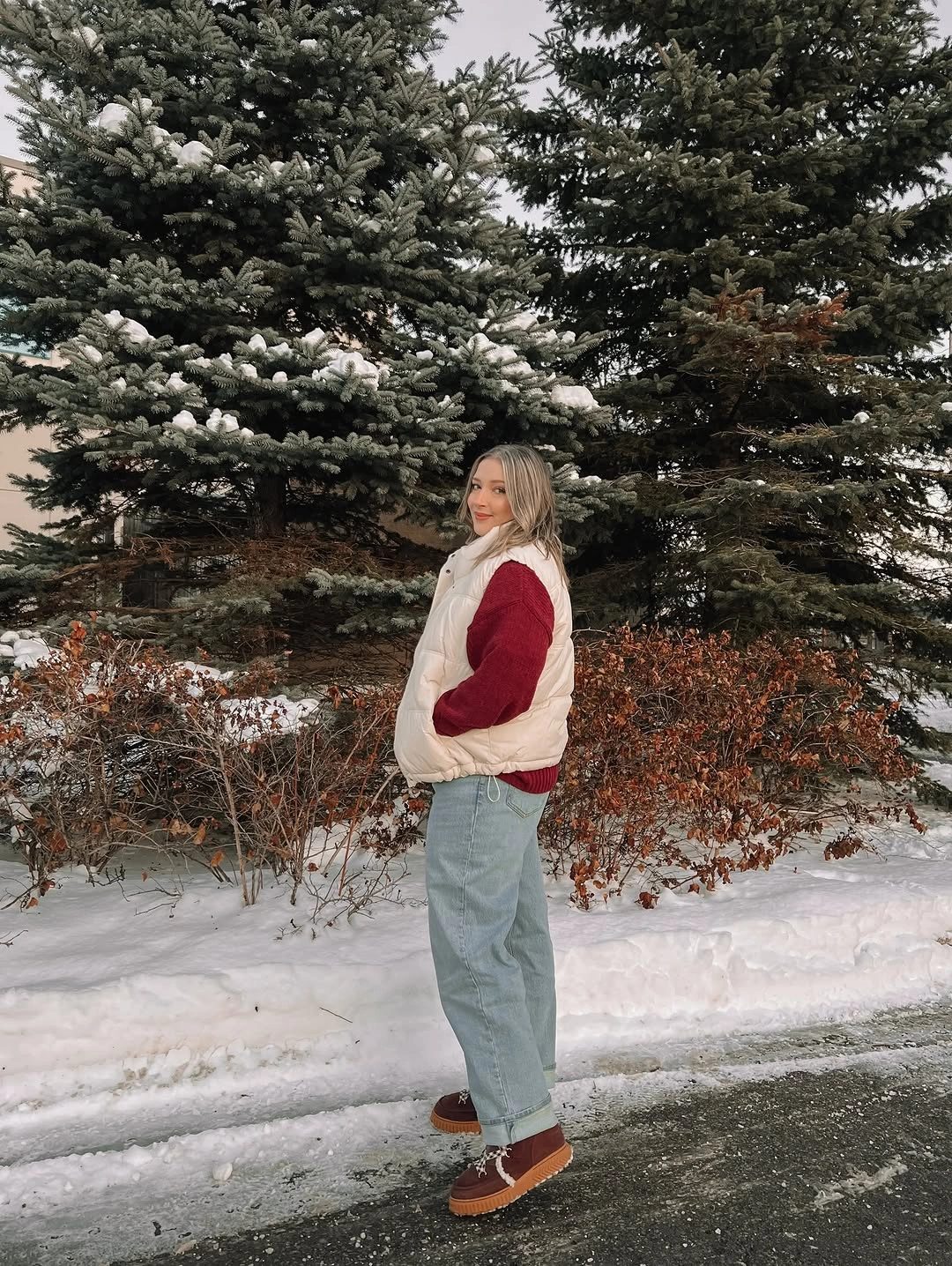 cream puffer vest over red sweater with light blue jeans and brown low shoes