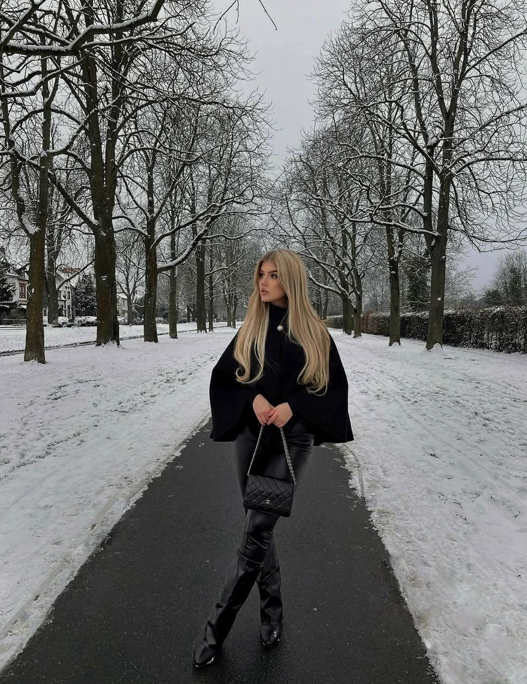 wide black cape-like outer layer with tall black boots and quilted handbag