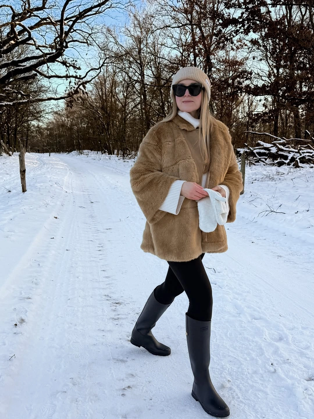 tan textured jacket with black leggings tall black boots and cream beanie