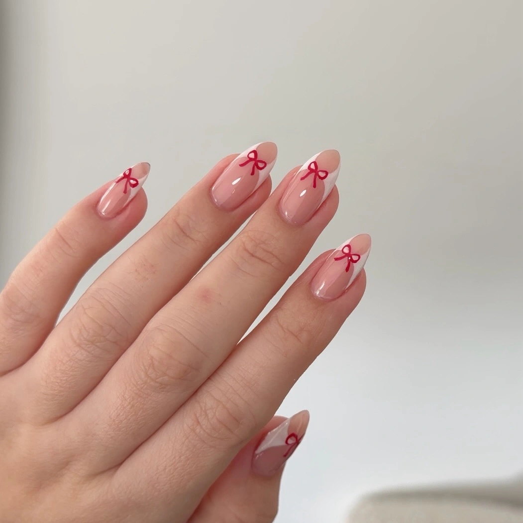 Short nude-pink almond nails with tiny red bow outlines