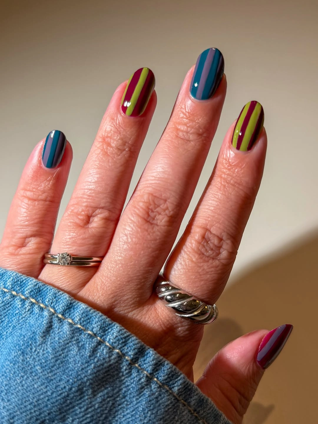 Short rounded nails with glossy teal and raspberry vertical stripes
