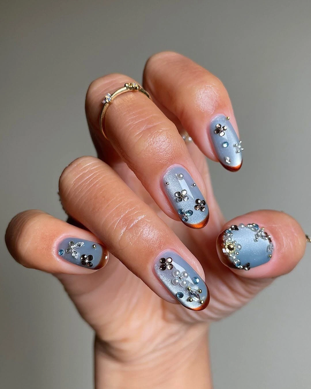 Short light blue nails with raised metallic and pearl accents